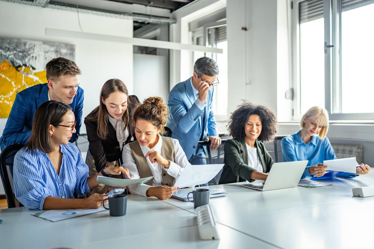 Diverse group of professionals discussing documents and ideas around a conference table, actively engaged in a brainstorming session, fostering teamwork and productivity